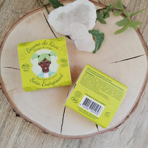 Baume de kiwi bio dans son pot, entouré de morceaux de kiwi frais et fleurs séchées sur fond clair