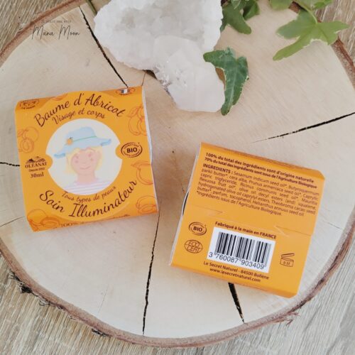 Baume d’abricot bio dans un pot en verre ambré, posé sur un tissu clair avec noyaux d’abricot et fleurs séchées autour