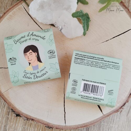 Baume à l’amande douce dans son pot en verre, entouré de fleurs de coton et d’amandes, sur un fond beige doux