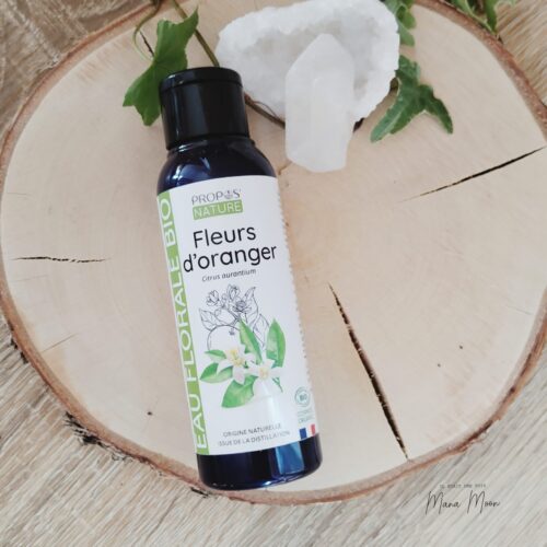 Flacon d’hydrolat de fleurs d’oranger posé sur un linge blanc, entouré de petites fleurs blanches